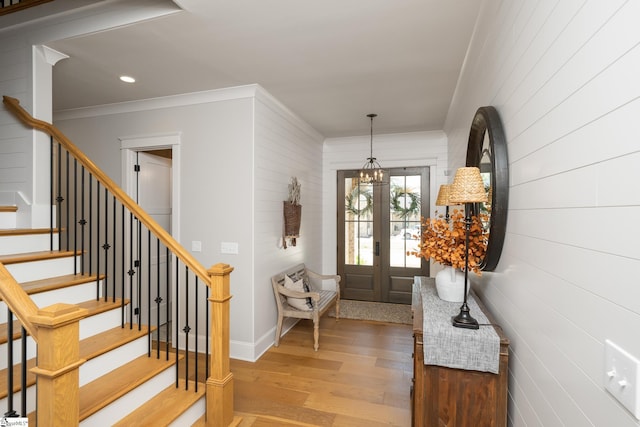 foyer entrance featuring crown molding, light hardwood / wood-style flooring, french doors, and a notable chandelier