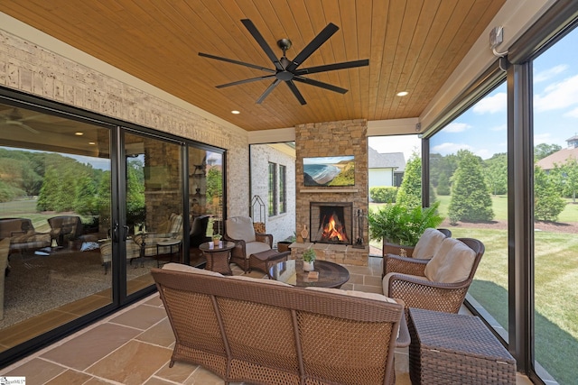 sunroom with ceiling fan, plenty of natural light, wooden ceiling, and an outdoor stone fireplace