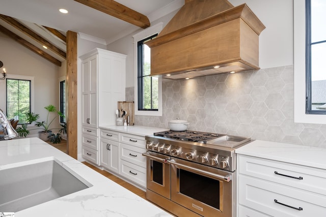 kitchen featuring light stone countertops, sink, range with two ovens, decorative backsplash, and custom range hood