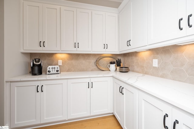 kitchen with decorative backsplash, light hardwood / wood-style floors, white cabinetry, and light stone counters