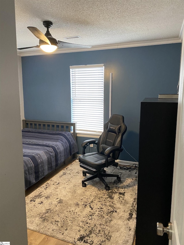 bedroom with ceiling fan, wood-type flooring, a textured ceiling, and ornamental molding