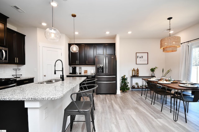 kitchen with sink, a kitchen island with sink, stainless steel appliances, and hanging light fixtures