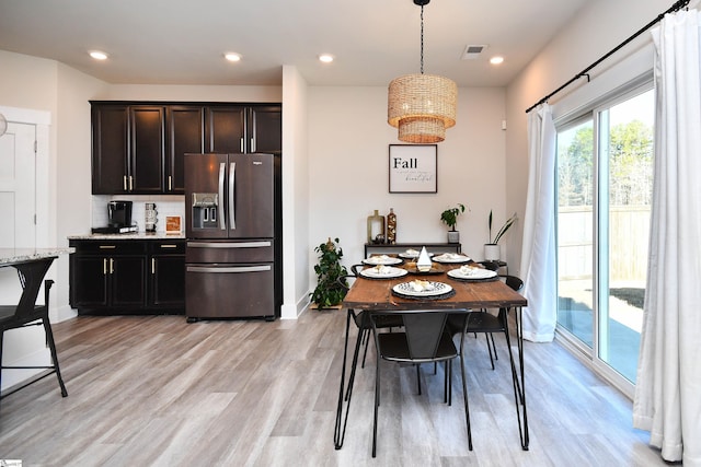 kitchen featuring stainless steel refrigerator with ice dispenser, hanging light fixtures, decorative backsplash, light wood-type flooring, and dark brown cabinets