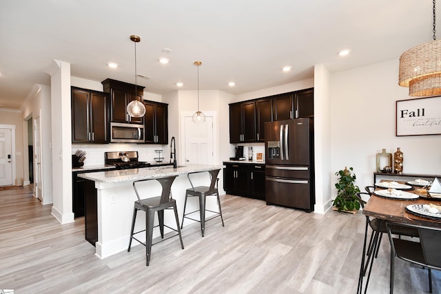 kitchen featuring light stone countertops, decorative backsplash, stainless steel appliances, decorative light fixtures, and a center island with sink