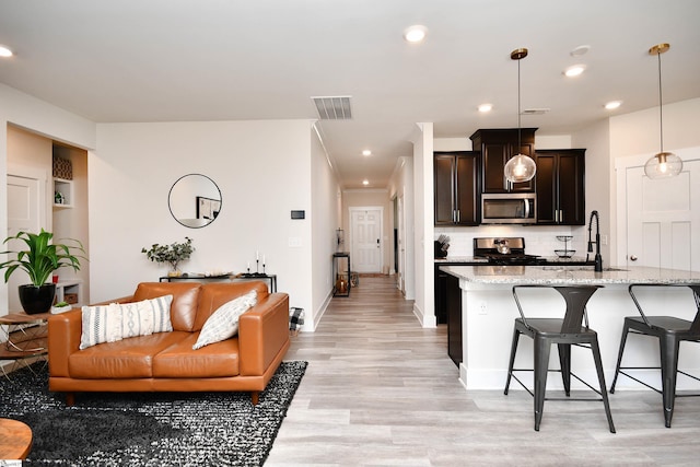 kitchen with light stone countertops, appliances with stainless steel finishes, decorative light fixtures, dark brown cabinetry, and a breakfast bar area