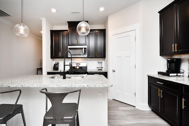 kitchen featuring backsplash, a breakfast bar, decorative light fixtures, and a center island with sink