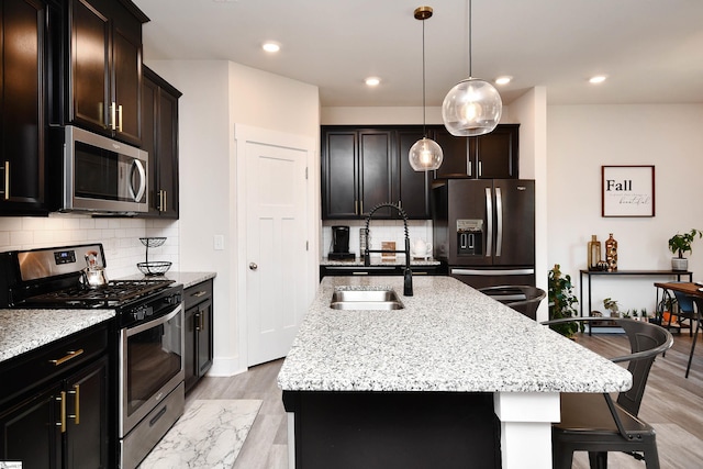 kitchen featuring a kitchen island with sink, decorative backsplash, light stone countertops, decorative light fixtures, and stainless steel appliances