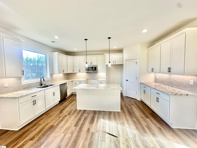 kitchen with a sink, a kitchen island, white cabinetry, hanging light fixtures, and appliances with stainless steel finishes