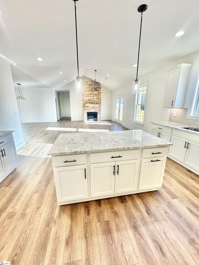 kitchen featuring white cabinets, light wood-style flooring, light stone counters, and open floor plan