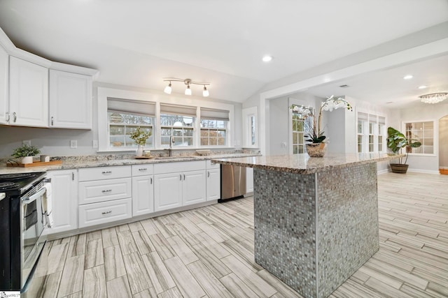 kitchen featuring stove, white cabinets, sink, light stone countertops, and a kitchen island