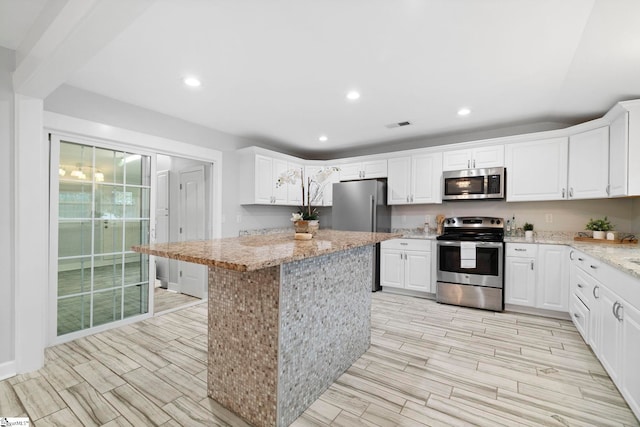 kitchen featuring light stone counters, a center island, white cabinets, and stainless steel appliances