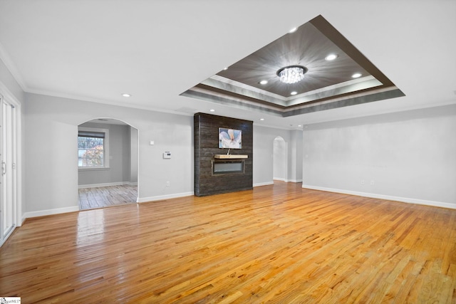 unfurnished living room featuring a raised ceiling, a brick fireplace, crown molding, and light wood-type flooring