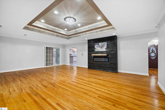 unfurnished living room with a raised ceiling, crown molding, light hardwood / wood-style flooring, and a chandelier