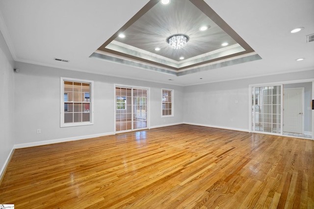 empty room featuring a tray ceiling, light hardwood / wood-style floors, ornamental molding, and a notable chandelier