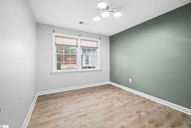 spare room with light wood-type flooring and a notable chandelier