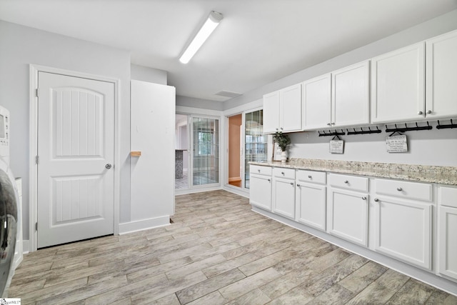 kitchen with light hardwood / wood-style floors, white cabinetry, stacked washer and clothes dryer, and light stone counters