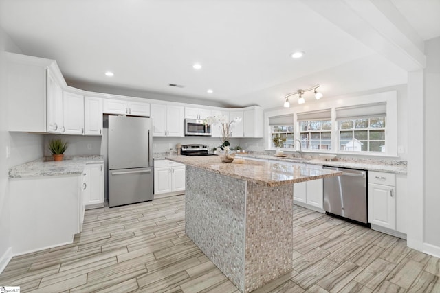 kitchen featuring white cabinets, a center island, light stone countertops, and appliances with stainless steel finishes