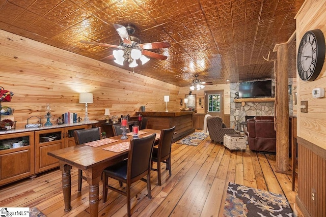 dining room with wood walls, ceiling fan, light hardwood / wood-style floors, and a fireplace