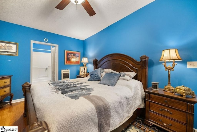 bedroom featuring ensuite bath, a textured ceiling, heating unit, ceiling fan, and hardwood / wood-style flooring