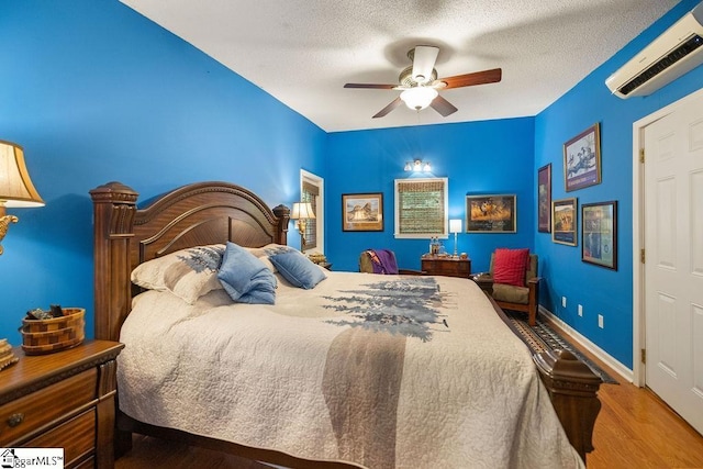 bedroom featuring ceiling fan, wood-type flooring, a textured ceiling, and a wall unit AC