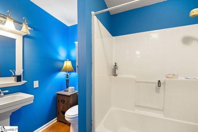 full bathroom with  shower combination, sink, hardwood / wood-style flooring, toilet, and a textured ceiling