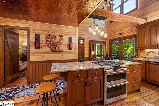 kitchen featuring light stone countertops, pendant lighting, double oven range, a breakfast bar area, and wood walls