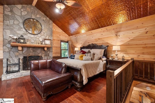 bedroom featuring high vaulted ceiling, a stone fireplace, wood-type flooring, and wooden walls