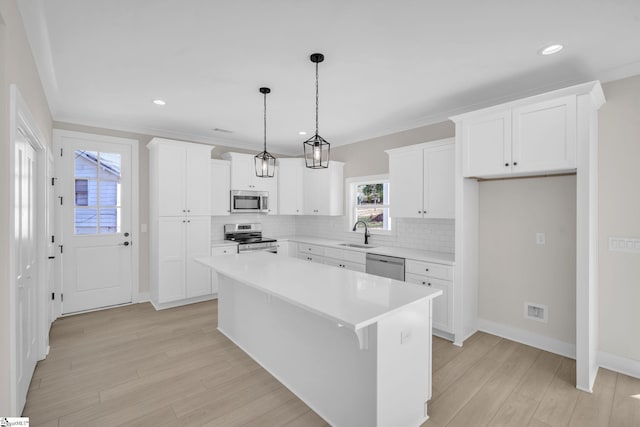 kitchen with white cabinets, a kitchen island, decorative light fixtures, and appliances with stainless steel finishes