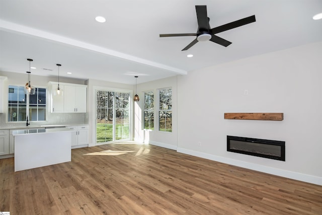 unfurnished living room with beamed ceiling, light wood-type flooring, ceiling fan, and sink