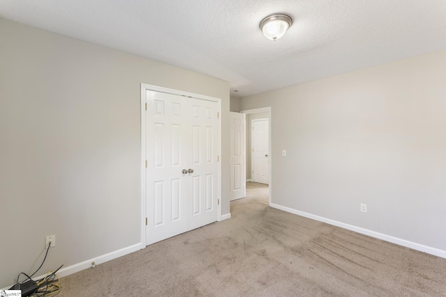 unfurnished bedroom with a textured ceiling, light colored carpet, and a closet