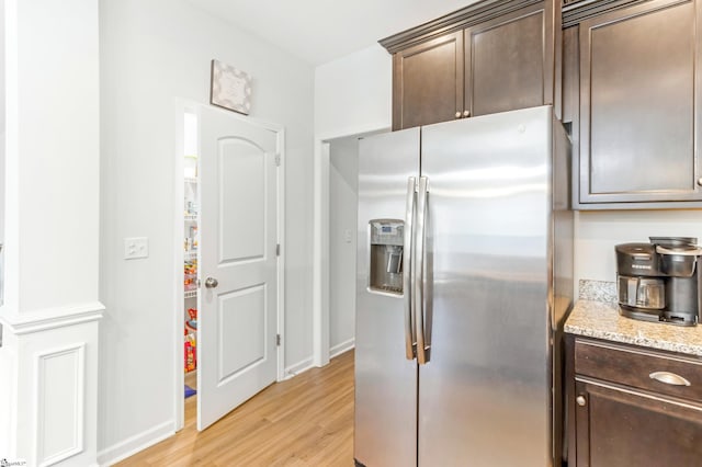 kitchen with stainless steel fridge, light hardwood / wood-style floors, light stone counters, and dark brown cabinets