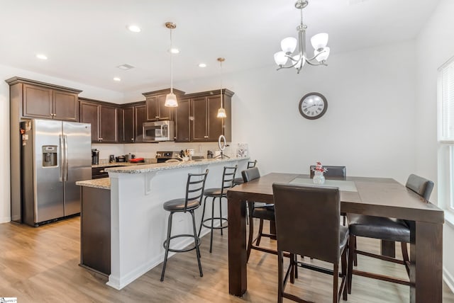 kitchen with pendant lighting, an inviting chandelier, light hardwood / wood-style flooring, kitchen peninsula, and stainless steel appliances