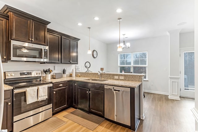 kitchen with decorative light fixtures, light wood-type flooring, kitchen peninsula, and stainless steel appliances