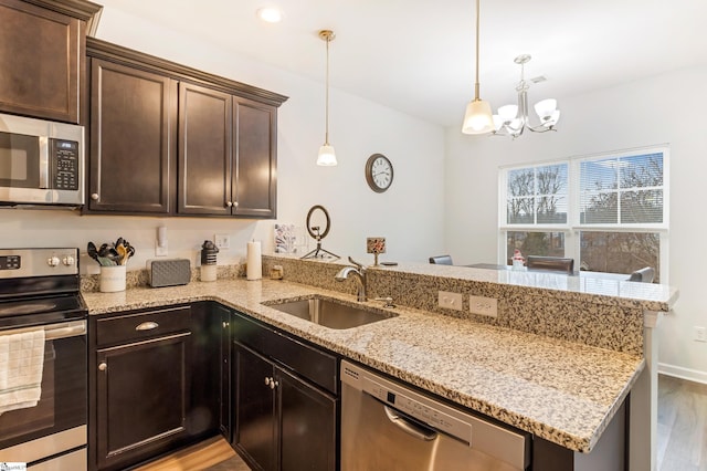 kitchen with kitchen peninsula, appliances with stainless steel finishes, dark brown cabinetry, sink, and pendant lighting