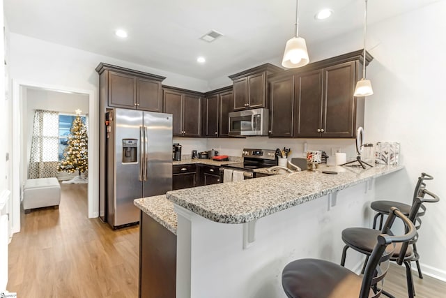 kitchen with pendant lighting, light hardwood / wood-style floors, a kitchen bar, kitchen peninsula, and stainless steel appliances