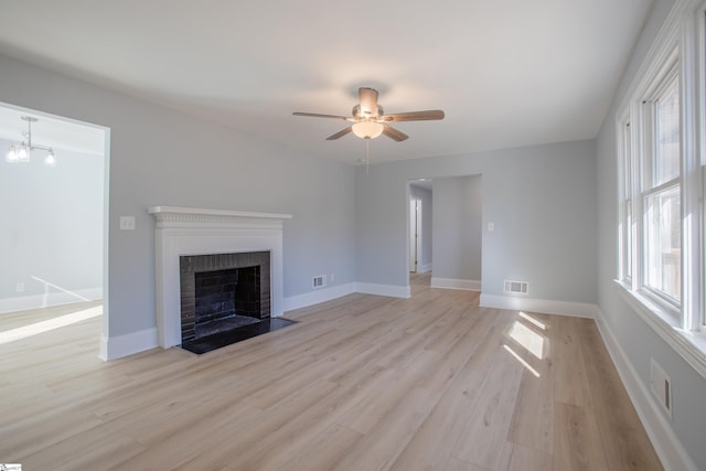 unfurnished living room with ceiling fan with notable chandelier, light hardwood / wood-style floors, and a fireplace