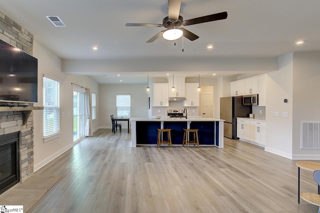 kitchen with pendant lighting, white cabinets, a brick fireplace, appliances with stainless steel finishes, and light hardwood / wood-style floors