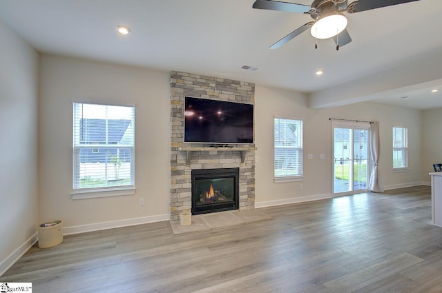 unfurnished living room featuring ceiling fan, a stone fireplace, and light hardwood / wood-style flooring