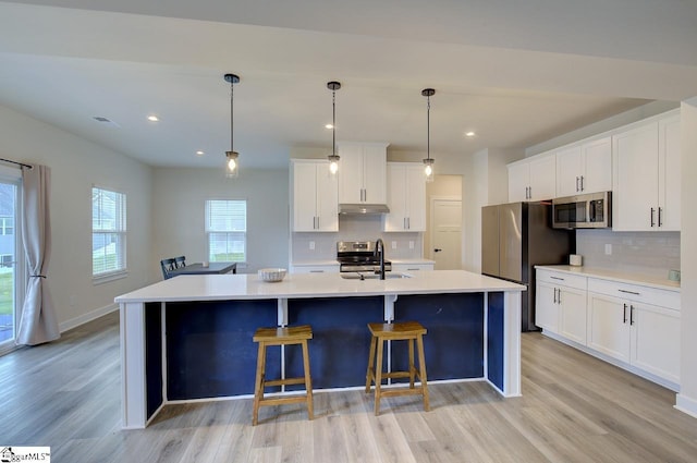 kitchen with white cabinetry, sink, stainless steel appliances, decorative light fixtures, and a kitchen island with sink