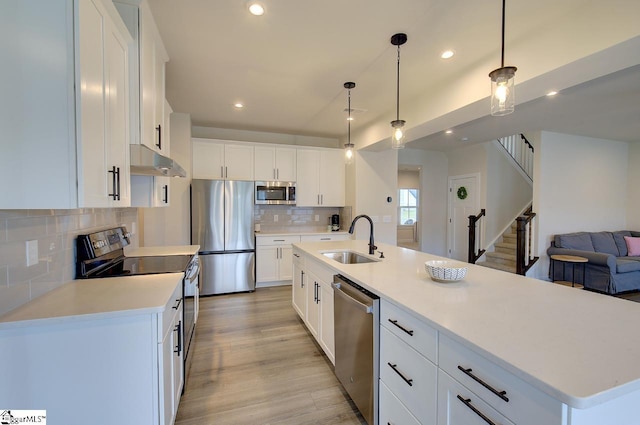 kitchen with decorative backsplash, appliances with stainless steel finishes, a kitchen island with sink, sink, and white cabinets