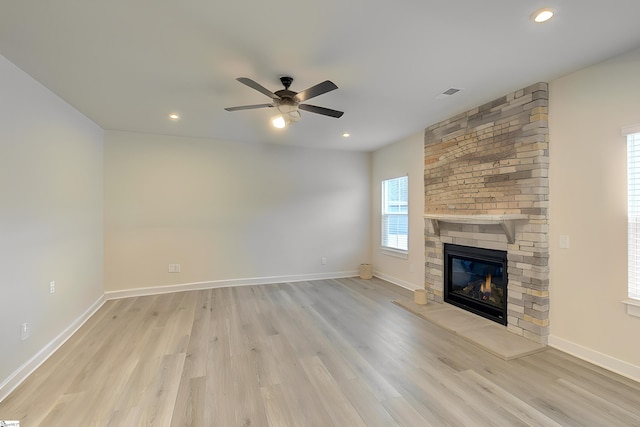 unfurnished living room featuring a stone fireplace, ceiling fan, plenty of natural light, and light hardwood / wood-style flooring