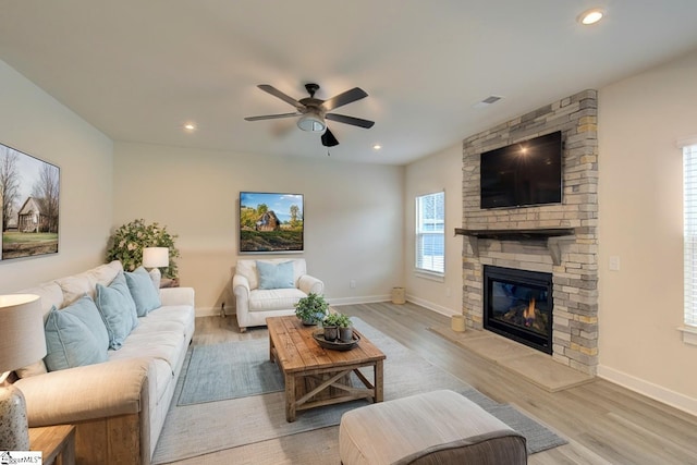 living room with light wood-type flooring, a stone fireplace, and ceiling fan