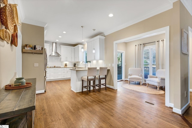 kitchen with kitchen peninsula, a kitchen breakfast bar, wall chimney exhaust hood, white cabinets, and hanging light fixtures