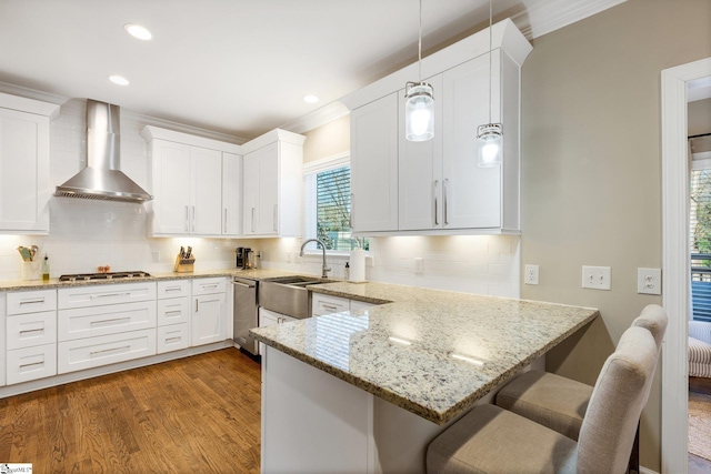 kitchen with white cabinets, a breakfast bar, hanging light fixtures, and wall chimney exhaust hood