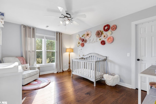 bedroom featuring a crib, ceiling fan, and dark wood-type flooring