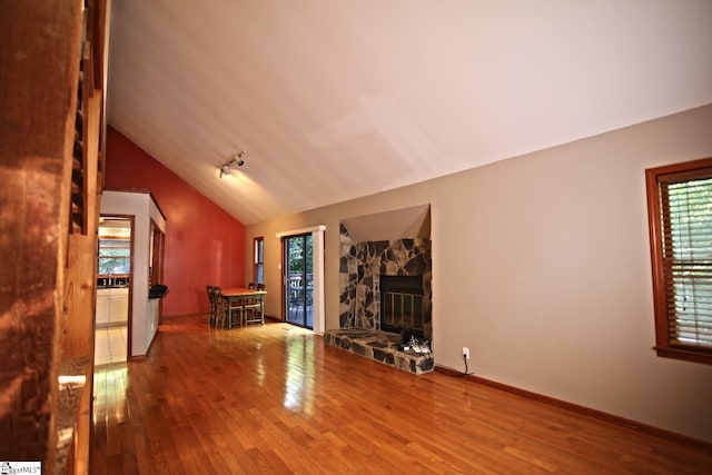 unfurnished living room with a stone fireplace, hardwood / wood-style floors, and vaulted ceiling