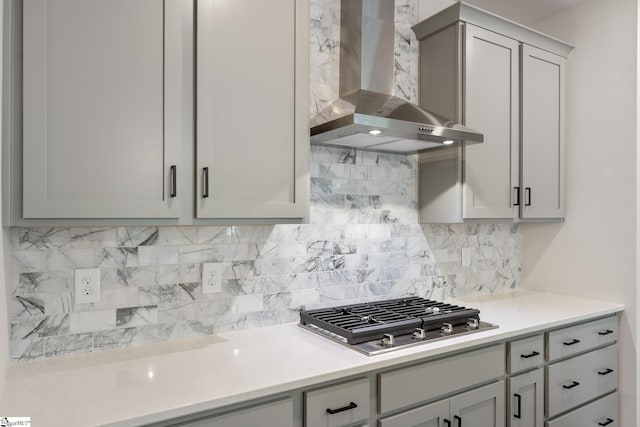 kitchen featuring stainless steel gas cooktop, wall chimney range hood, gray cabinetry, and decorative backsplash