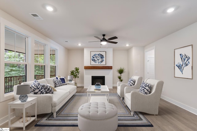 living room featuring hardwood / wood-style floors, ceiling fan, and a large fireplace