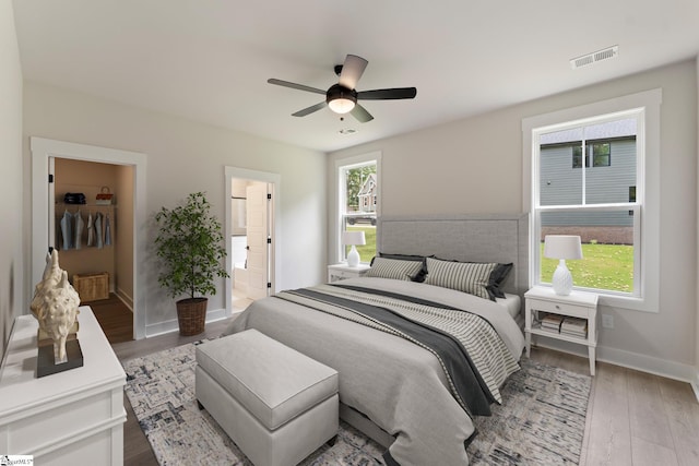 bedroom featuring ceiling fan, light hardwood / wood-style flooring, ensuite bath, and a spacious closet