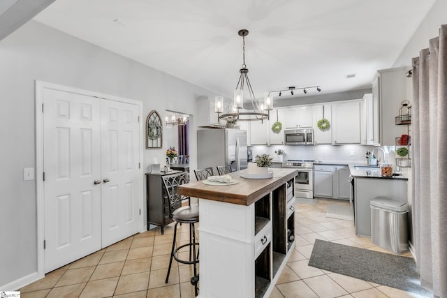 kitchen with light tile patterned floors, butcher block countertops, pendant lighting, a kitchen island, and appliances with stainless steel finishes